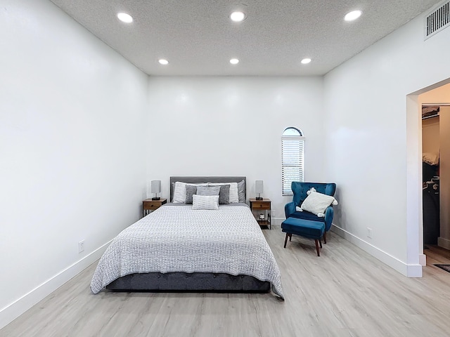 bedroom with a spacious closet, light hardwood / wood-style floors, and a textured ceiling