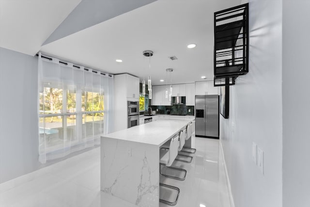 kitchen with a kitchen island, appliances with stainless steel finishes, decorative light fixtures, white cabinets, and a kitchen breakfast bar