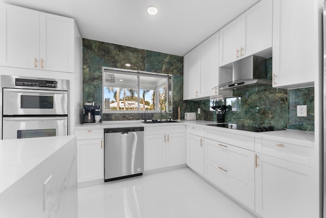 kitchen featuring appliances with stainless steel finishes, sink, white cabinets, decorative backsplash, and wall chimney exhaust hood