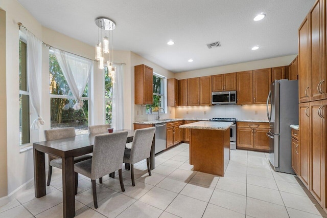 kitchen featuring sink, appliances with stainless steel finishes, hanging light fixtures, a center island, and light tile patterned flooring