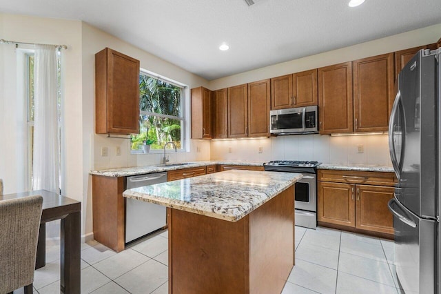 kitchen featuring light tile patterned flooring, a kitchen island, sink, light stone counters, and stainless steel appliances