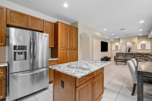 kitchen featuring light tile patterned floors, stainless steel fridge, light stone countertops, and a kitchen island