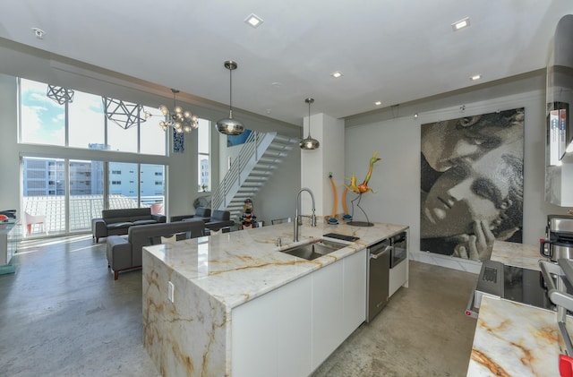 kitchen featuring pendant lighting, sink, white cabinetry, light stone countertops, and an island with sink