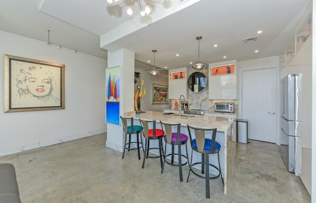 kitchen with a breakfast bar area, white cabinetry, decorative light fixtures, stainless steel fridge, and kitchen peninsula