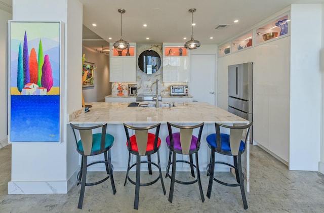 kitchen with white cabinetry, hanging light fixtures, light stone counters, and stainless steel fridge