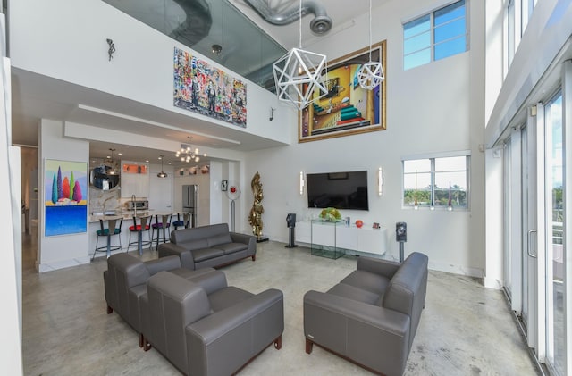 living room with an inviting chandelier, a towering ceiling, and concrete floors