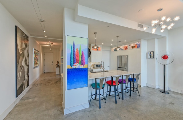 kitchen with sink, stainless steel fridge, a breakfast bar, white cabinetry, and hanging light fixtures