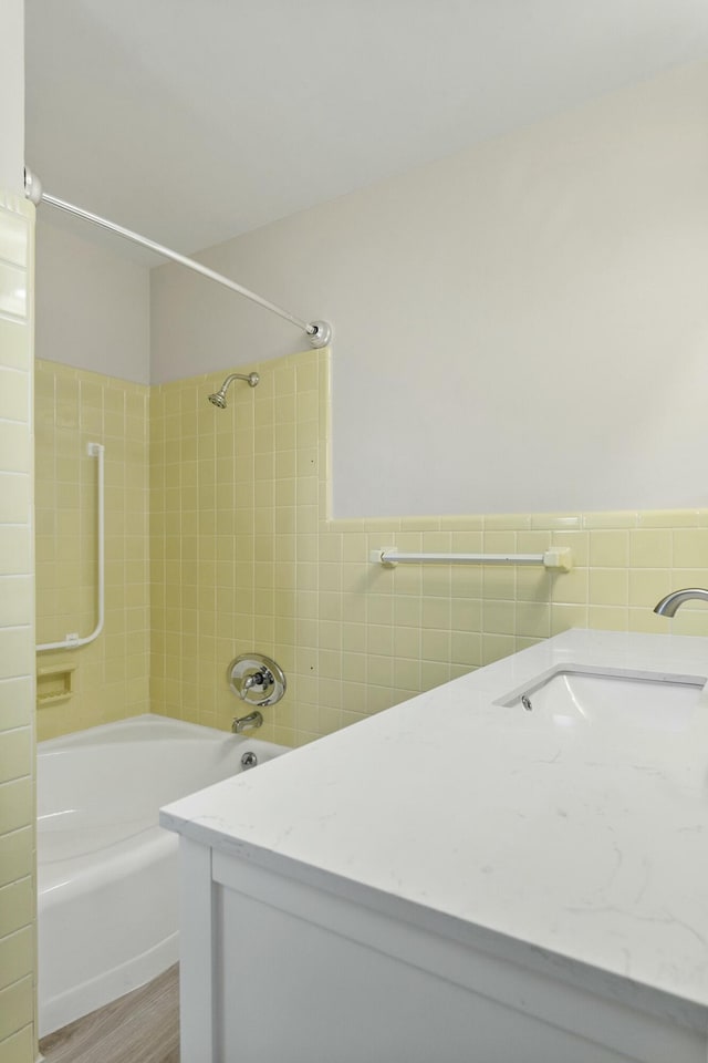 bathroom with hardwood / wood-style flooring, tiled shower / bath, sink, and tile walls