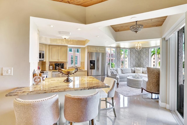 kitchen featuring light stone counters, appliances with stainless steel finishes, a breakfast bar area, and cream cabinetry