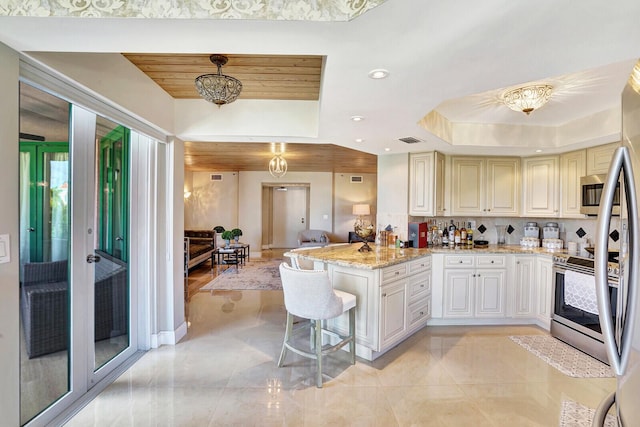 kitchen featuring a breakfast bar, stainless steel appliances, light stone counters, a tray ceiling, and decorative light fixtures