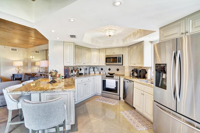 kitchen featuring a breakfast bar, stainless steel appliances, light stone counters, decorative backsplash, and a raised ceiling