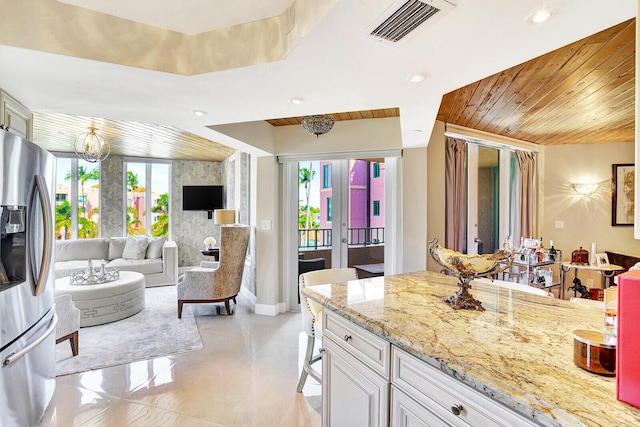 kitchen featuring white cabinets, light stone countertops, plenty of natural light, and stainless steel fridge