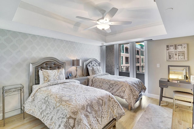 bedroom with ceiling fan, a raised ceiling, light hardwood / wood-style floors, and access to outside