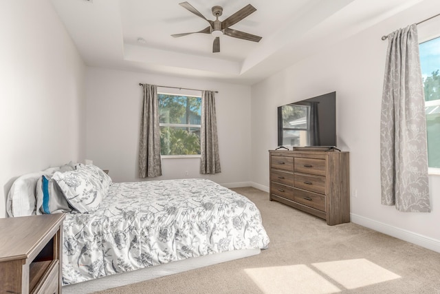 bedroom with light colored carpet, a raised ceiling, and ceiling fan