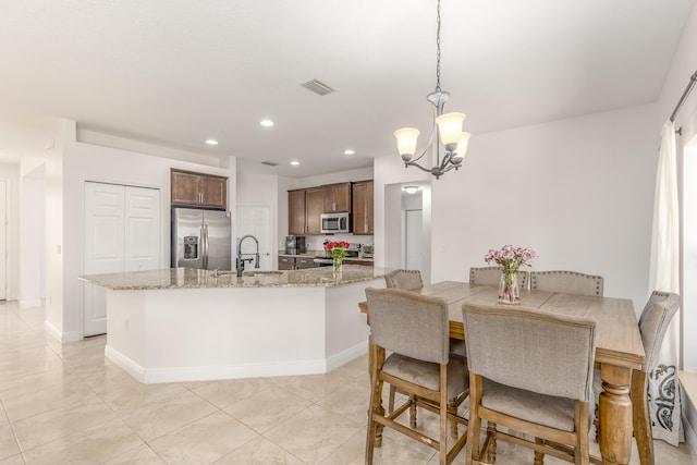 kitchen with sink, appliances with stainless steel finishes, hanging light fixtures, light stone counters, and a notable chandelier