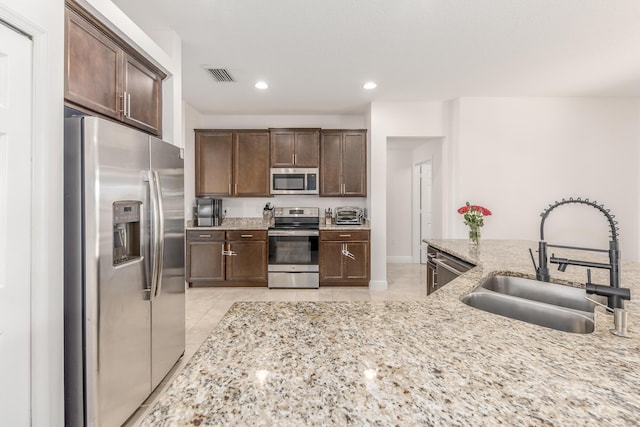 kitchen featuring light tile patterned flooring, sink, light stone counters, dark brown cabinets, and appliances with stainless steel finishes