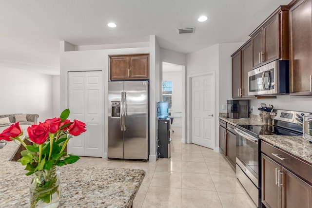 kitchen with dark brown cabinetry, a textured ceiling, light tile patterned floors, stainless steel appliances, and light stone countertops