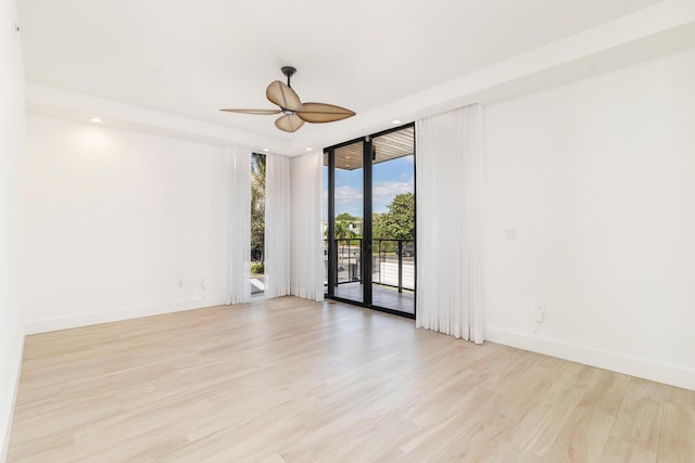 empty room with ceiling fan, a wall of windows, and light hardwood / wood-style floors