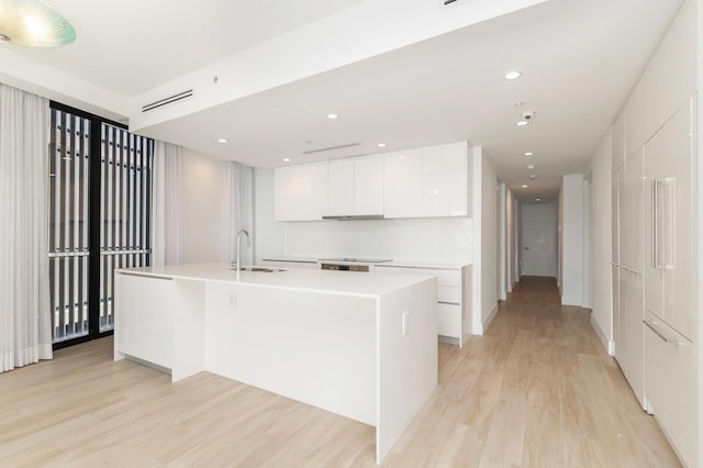 kitchen featuring white cabinetry, sink, light hardwood / wood-style flooring, and an island with sink