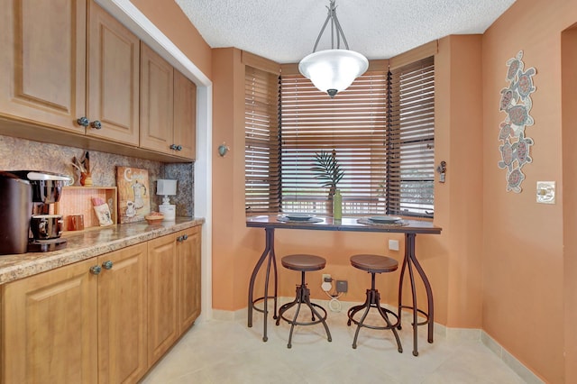 interior space featuring hanging light fixtures, light stone countertops, a textured ceiling, and decorative backsplash