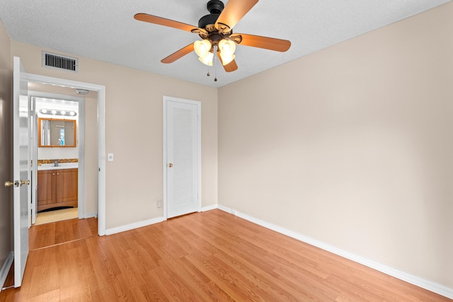 unfurnished bedroom featuring sink, a textured ceiling, light wood-type flooring, a closet, and ceiling fan