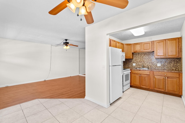 kitchen featuring sink, decorative backsplash, light tile patterned floors, white appliances, and a textured ceiling