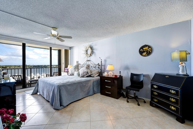 bedroom with a water view, light tile patterned floors, access to exterior, and a wall of windows