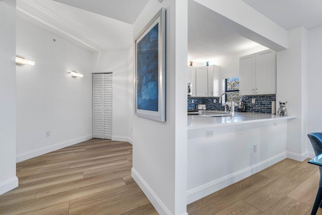 kitchen with white cabinetry, sink, decorative backsplash, and light wood-type flooring