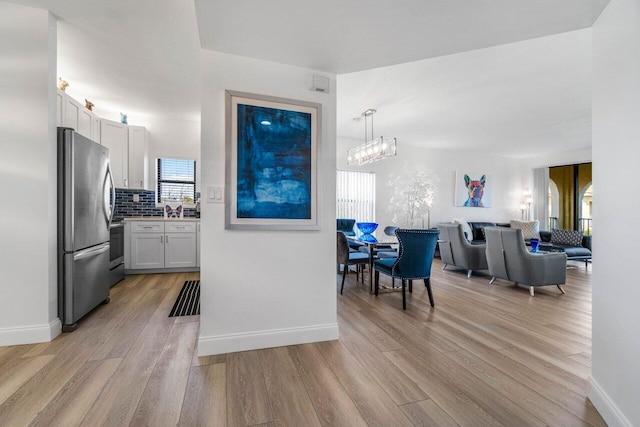 kitchen with stainless steel refrigerator, white cabinetry, decorative light fixtures, and light hardwood / wood-style flooring