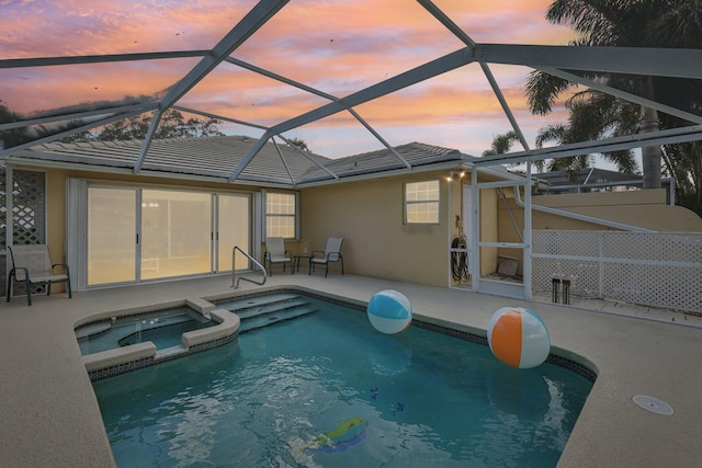 pool at dusk featuring a lanai, a patio, and a pool with connected hot tub