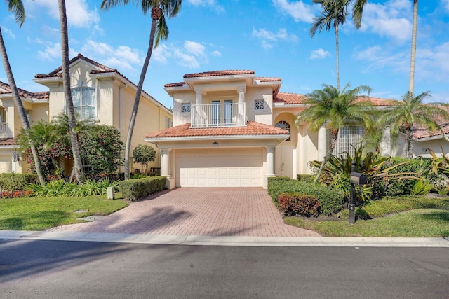 mediterranean / spanish house with decorative driveway, stucco siding, a balcony, a garage, and a tiled roof