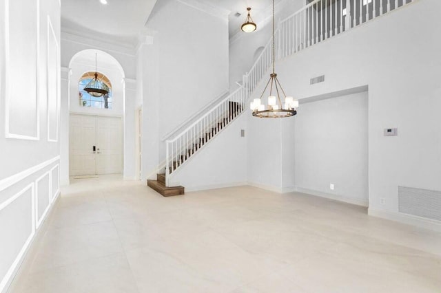 entryway with crown molding, a notable chandelier, a towering ceiling, and light tile patterned floors