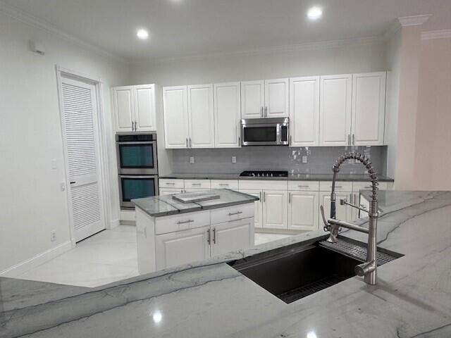 kitchen with sink, white cabinetry, stainless steel appliances, light stone countertops, and decorative backsplash