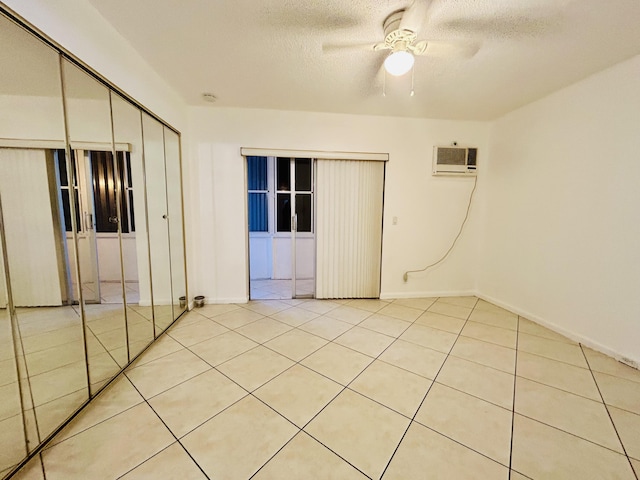 unfurnished bedroom featuring light tile patterned flooring, a wall mounted AC, a textured ceiling, a closet, and ceiling fan