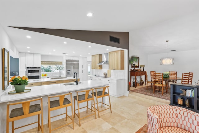 kitchen with appliances with stainless steel finishes, decorative light fixtures, sink, a center island with sink, and wall chimney exhaust hood