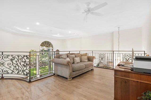 living room featuring ceiling fan with notable chandelier, a raised ceiling, and light wood-type flooring