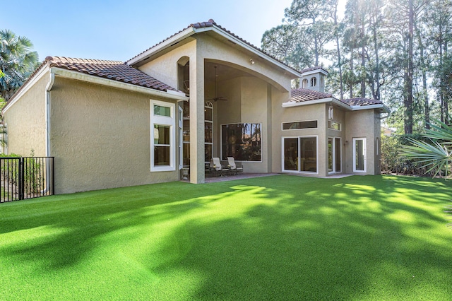 rear view of property featuring ceiling fan and a lawn