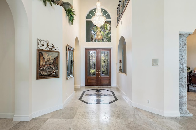 foyer with a notable chandelier, a towering ceiling, and french doors