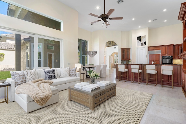 tiled living room with a towering ceiling and ceiling fan with notable chandelier