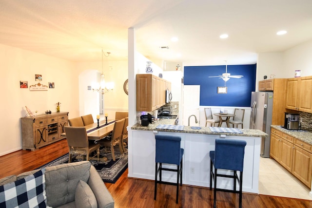 kitchen featuring a kitchen bar, light stone counters, hanging light fixtures, kitchen peninsula, and stainless steel appliances