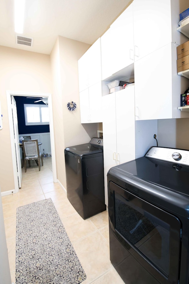 laundry area featuring separate washer and dryer, light tile patterned floors, and cabinets