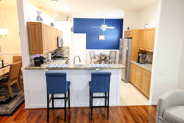 kitchen with a breakfast bar area, light stone countertops, kitchen peninsula, and appliances with stainless steel finishes