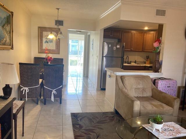 kitchen with pendant lighting, light tile patterned floors, sink, stainless steel fridge, and ornamental molding