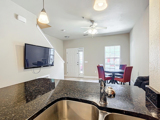 kitchen featuring sink, light tile patterned floors, pendant lighting, ceiling fan, and dark stone counters