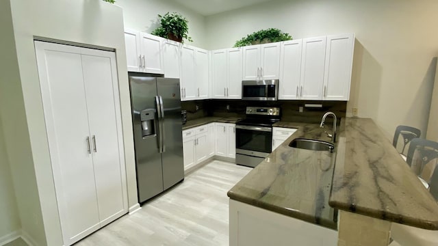 kitchen with appliances with stainless steel finishes, white cabinetry, sink, dark stone countertops, and light hardwood / wood-style floors