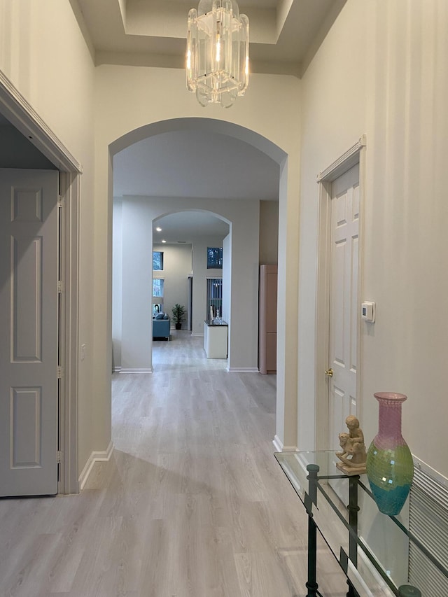 hall with a chandelier, light hardwood / wood-style floors, a raised ceiling, and a high ceiling