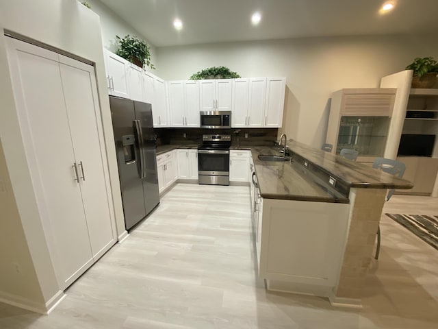 kitchen with sink, white cabinets, a kitchen breakfast bar, kitchen peninsula, and stainless steel appliances