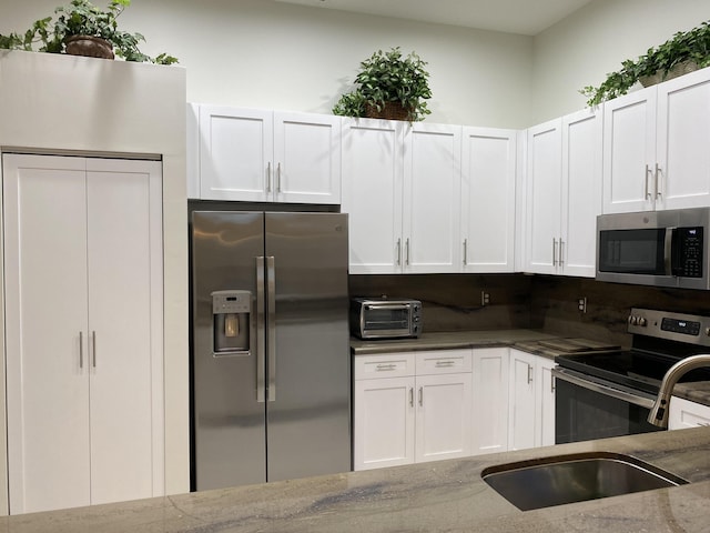 kitchen featuring stainless steel appliances, sink, white cabinets, and light stone counters