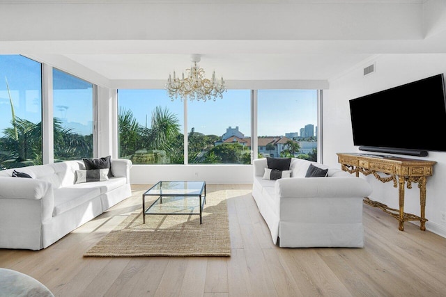 living area with light wood-type flooring, visible vents, and an inviting chandelier