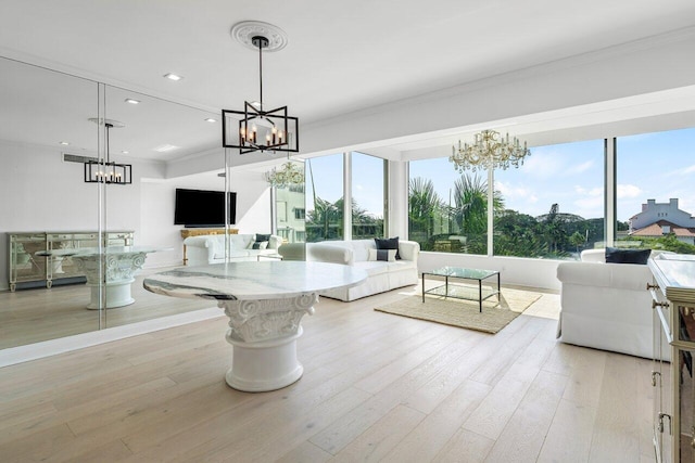 living area featuring a healthy amount of sunlight, crown molding, light wood-style flooring, and a notable chandelier